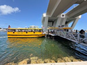 Bright yellow water taxi docked at a pier under a bridge