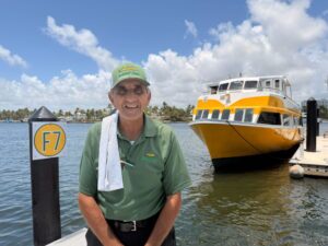 Man in green polo shirt stands on a dock with a yellow boat behind him.