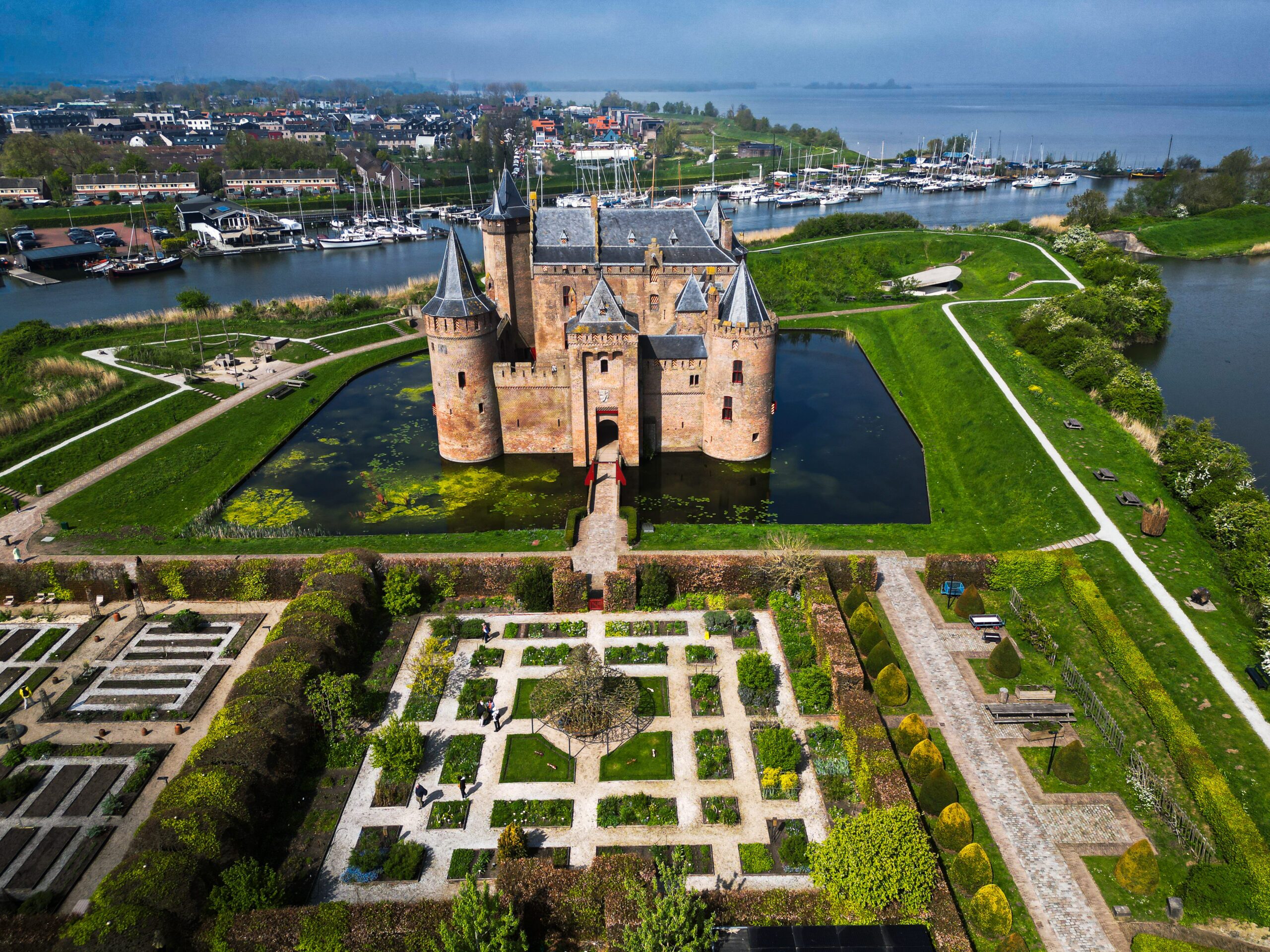 Flying view of Muiderslot Castle on a sunny spring day, showing its medieval structure, gardens, and water defenses