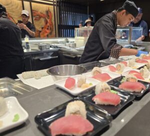 A black-clad sushi chef prepares a generous row of plates containing tuna nigiri and inside-out rolls on MSC Cruises' MSC World America. 