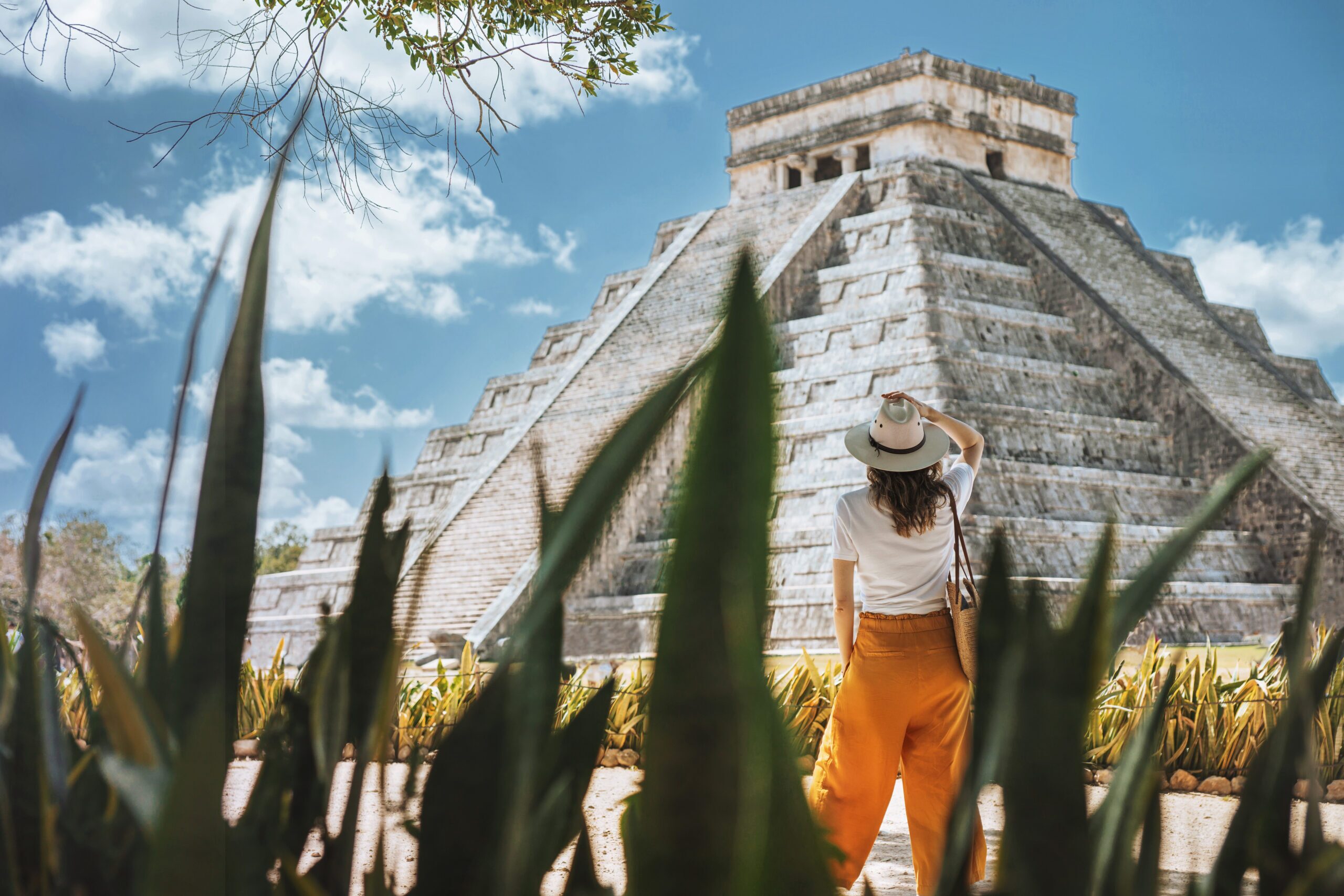 A young woman tourist in a hat stands against the background of the pyramid of Kukulcan in the ancient Mexican city of Chichen Itza. Travel concept