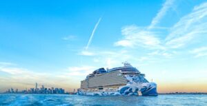 Norwegian Prima almost in silhouette on the horizon, blue sky behind, blue sea below, blue ship in the center.